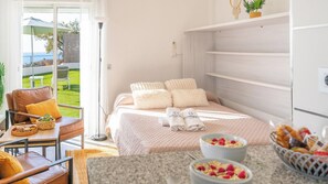 Un dormitorio con cama, almohadas, una mesita de noche con un tazón de cereal y vistas a un jardín.