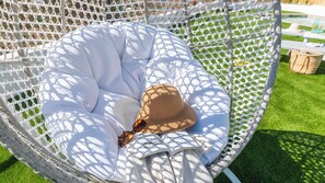 A white wicker chair with a white cushion, a straw hat, and sunglasses on it.