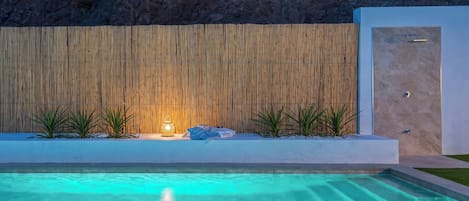 Ein Schwimmbecken mit Bambuswand im Hintergrund, ein kleiner Tisch mit einer Lampe und eine Tür rechts.