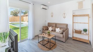Una sala de estar moderna con un sofá, una mesa de centro y un televisor. Hay un ventanal corredero que da a un jardín.