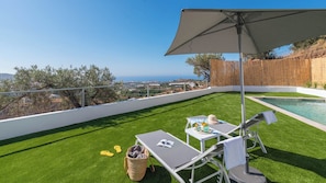 Terraza en la azotea con piscina, césped artificial verde, sillas de descanso y una mesa con bebidas y un sombrero.