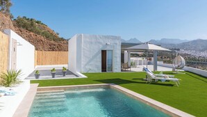 Un área de piscina exterior moderna con una vista despejada del paisaje circundante, incluyendo una cadena montañosa.
