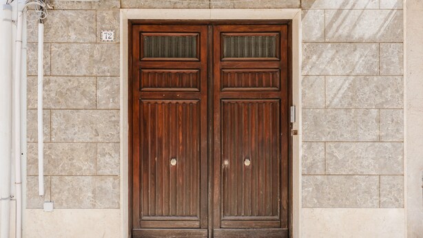 A double wooden door with a small window above it, set in a beige stone wall. - Holiday Home 'Iris Castelvetrano' with Wi-Fi and Air Conditioning (Castelvetrano)