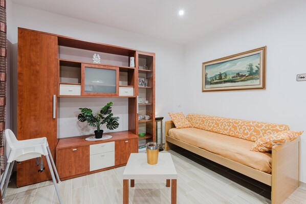 A living room with a wooden cabinet, a white sofa, a small table, and a potted plant.
