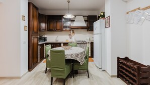 Una cocina con armarios de madera, una mesa de comedor con sillas verdes, un refrigerador blanco y una lámpara colgante.