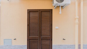 Puerta doble de madera con manija metálica, unidad de aire acondicionado de pared y un pequeño cuadro eléctrico a la izquierda.