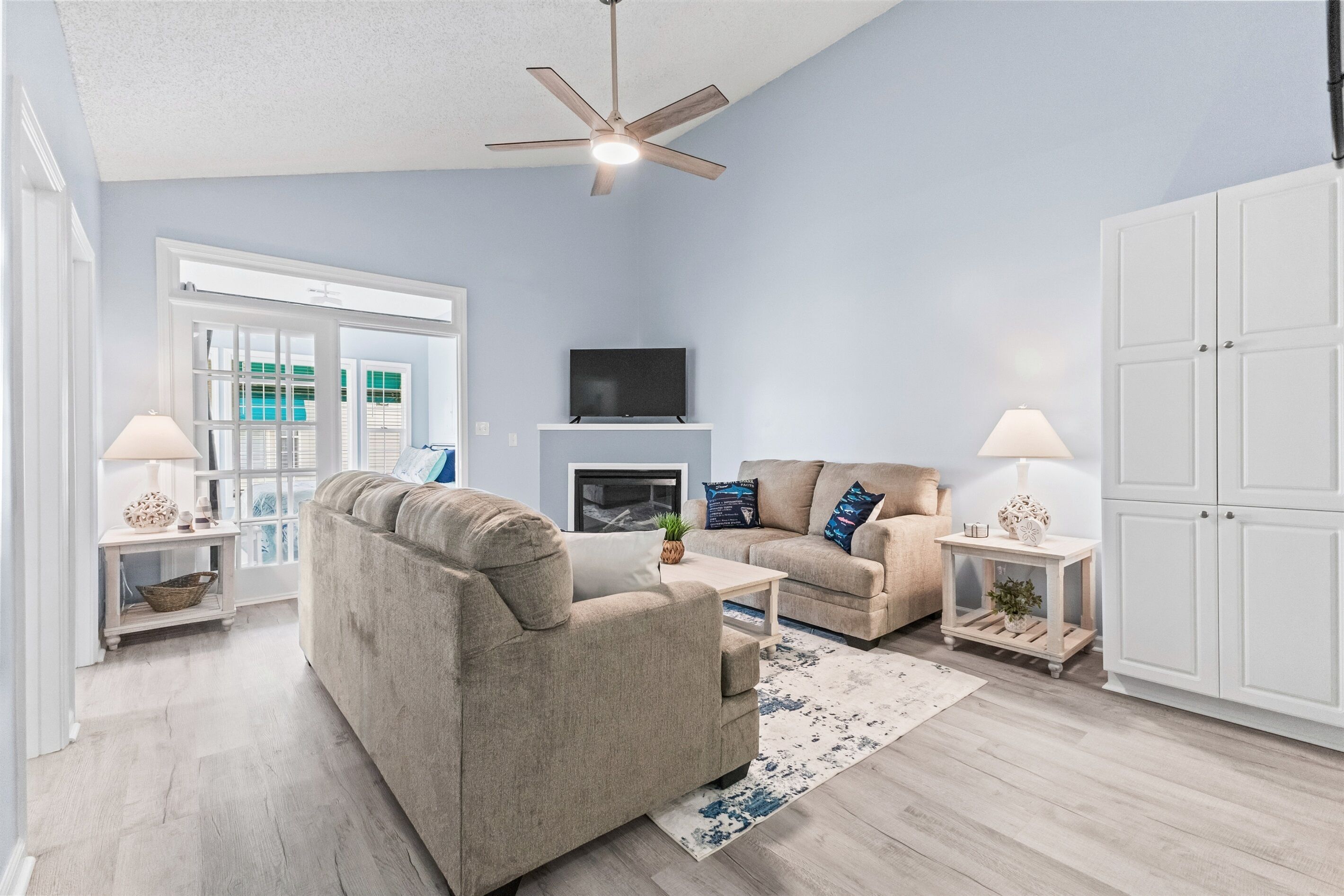 A living room with a sofa, coffee table, and two lamps. There is a television on a stand and a ceiling fan.