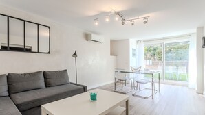 Una sala de estar moderna con un sofá gris, una mesa de centro blanca y un comedor con mesa y sillas de vidrio.