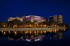 Un edificio moderno con la segnaletica 'STRAZ CENTER' che si riflette in una superficie d'acqua tranquilla, circondato da alberi e illuminato da lampioni.