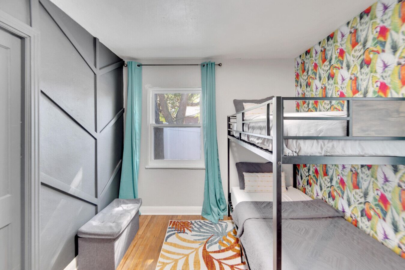 Une chambre avec un lit superposé, une fenêtre, des rideaux turquoise et un mur aux couleurs vives.