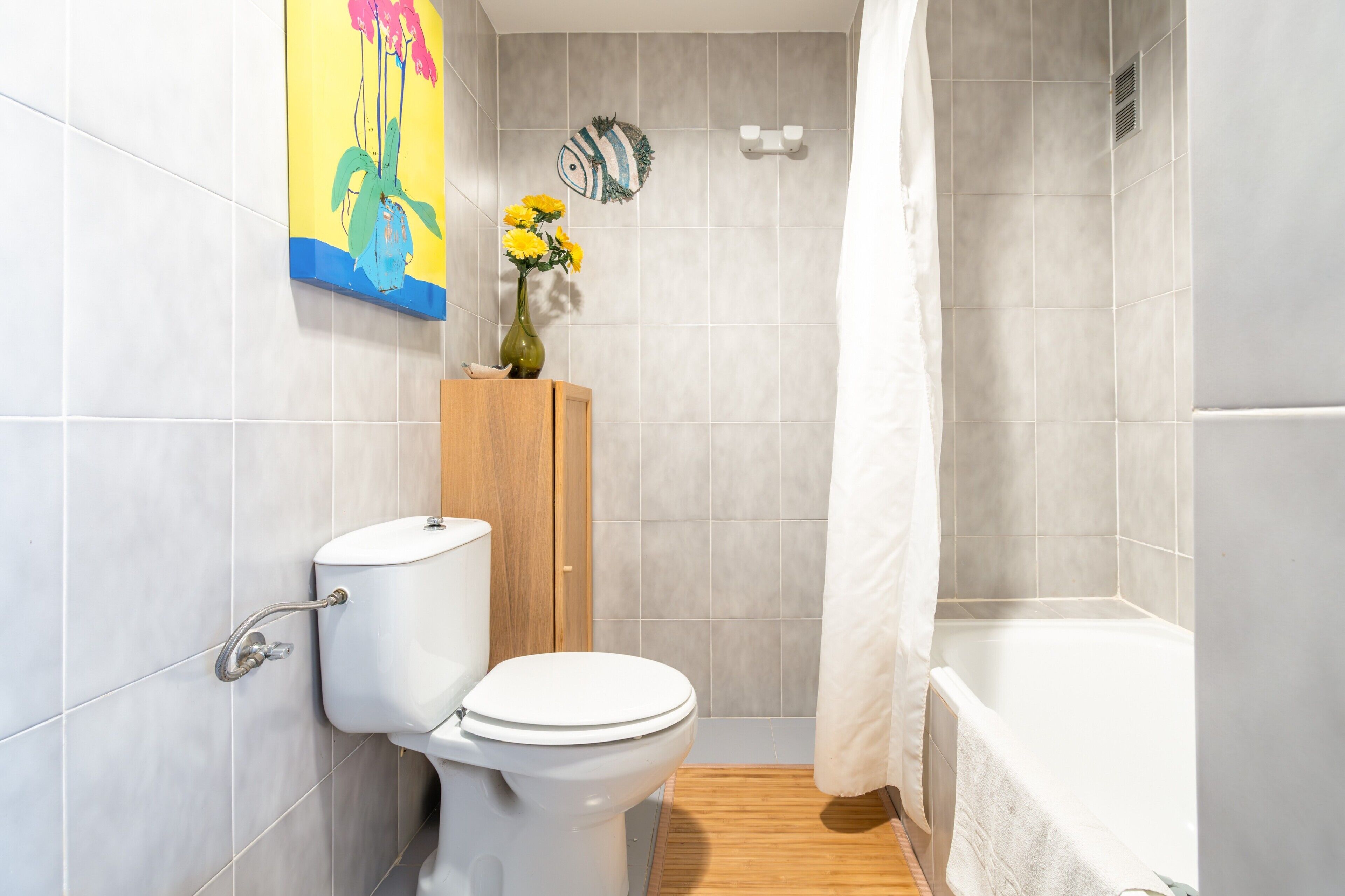 Un baño con inodoro, un armario de madera, cortina de ducha y pared con azulejos.