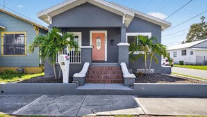 A two-story house with a front porch, a mailbox, and two palm trees.