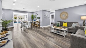 A modern living room with a dining area, grey walls, wooden flooring, and a view to a balcony. - Family Pool Home | Game Room + Fire Pit | Largo (Largo)