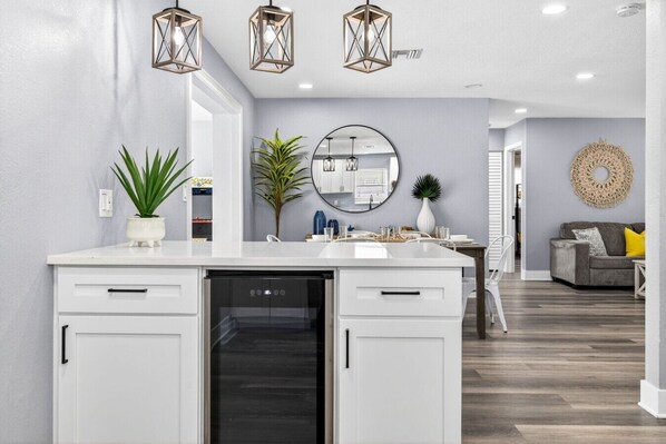 Une cuisine moderne avec des meubles blancs, un lave-vaisselle encastré et des luminaires suspendus.
