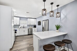 Une cuisine moderne avec des meubles blancs, des appareils en acier inoxydable et un îlot central doté de tabourets.
