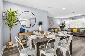 A modern living room with a dining area, a large mirror, and a potted plant.