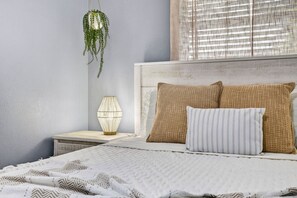 A bed with two pillows, a bedside lamp, and a hanging plant in a room with a plain wall and a window with blinds. - Family Pool Home | Game Room + Fire Pit | Largo (Largo)