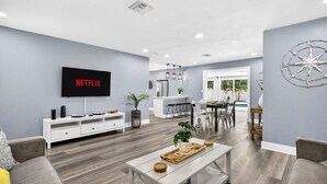 A modern living room with a flat-screen TV, a dining area, and a view of the outdoors. - Family Pool Home | Game Room + Fire Pit | Largo (Largo)