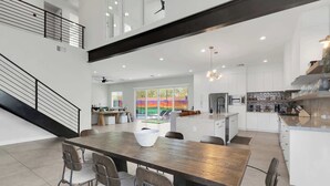 A spacious open-plan living area with a large wooden dining table, modern kitchen, and a staircase leading to an upper level. - Heated Pool & Spa, Golf Simulator, Billiards (Scottsdale)