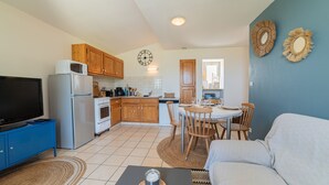 A compact kitchen with a microwave, refrigerator, and stove. There is a dining area with a table and chairs, and a living area with a sofa.