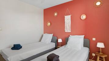 Habitación de hotel con dos camas, una pared de acento roja, lámparas de pared y un colgador de macramé.
