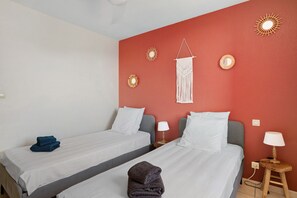 Habitación de hotel con dos camas, una pared de acento roja, lámparas de pared y un colgador de macramé.