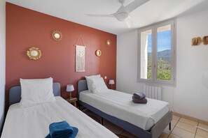 Habitación de hotel con dos camas, ventilador de techo, ventana con vistas y adornos en la pared.