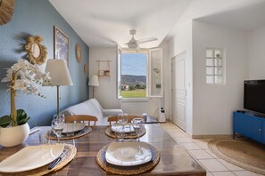 Un comedor con una mesa dispuesta para cuatro personas, un sofá y un televisor en una esquina.