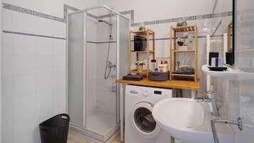 Een badkamer met een douche met glazen wand, een wasmachine, een wastafel en houten planken met toiletartikelen.