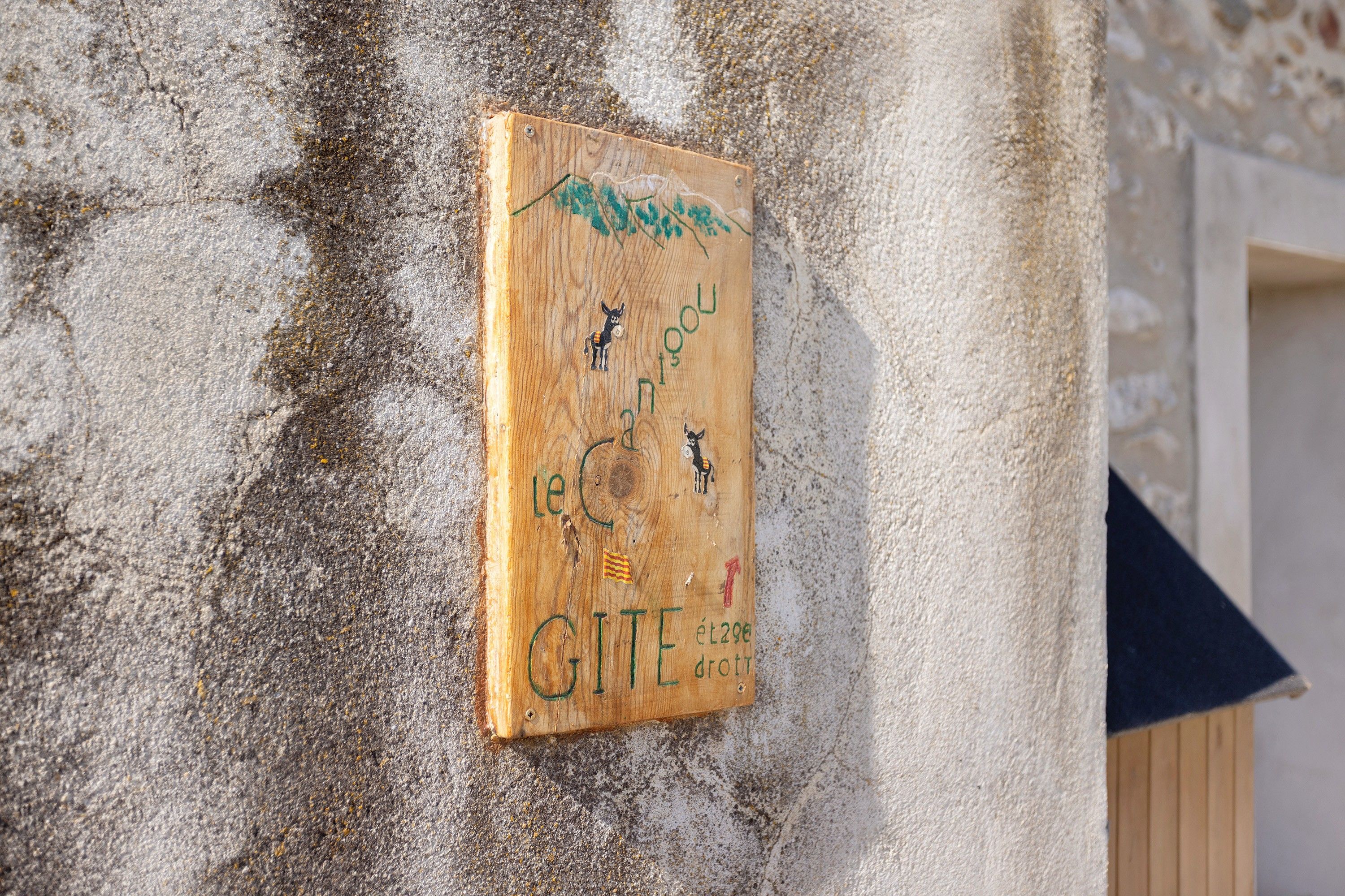 A wooden sign with text and symbols, mounted on a textured wall.