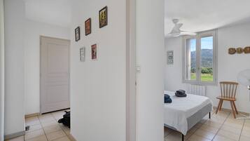 Een slaapkamer met een bed, een stoel, een raam met uitzicht en een plafondventilator.