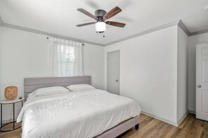A bedroom with a bed, a ceiling fan, a window with sheer curtains, and a door. - Downtown 5-Bedroom Oasis/Free Parking (Houston)