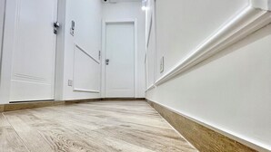 Corredor com paredes brancas, assoalho de madeira e uma porta fechada no final.