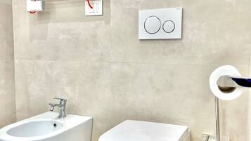 Un bagno con bidet, servizi igienici e pannello di controllo del bidet a parete.