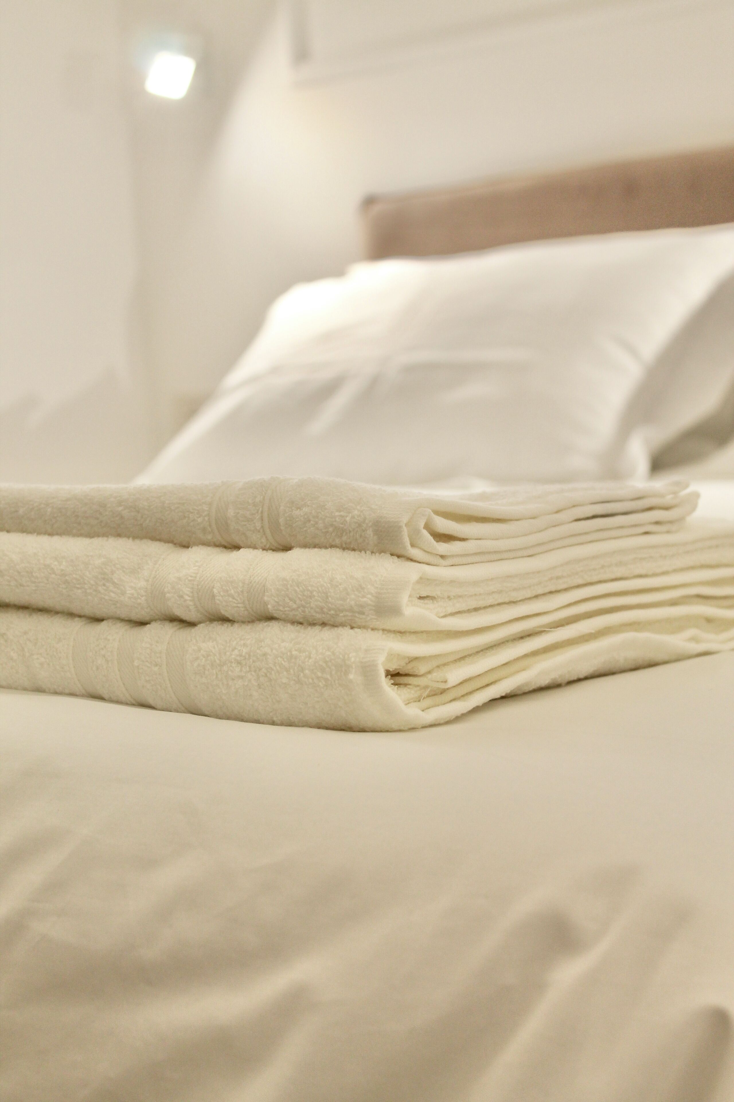 Ein ordentlich gemachtes Bett mit weißen Leinentüchern und einem Stapel gefalteter Handtücher.