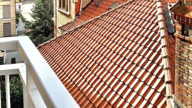 Terraço com telhas vermelhas, chaminé de tijolos e vista para o mar.