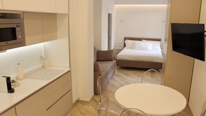 Quarto de hotel moderno com cozinha compacta, uma cama, televisão e área de jantar.