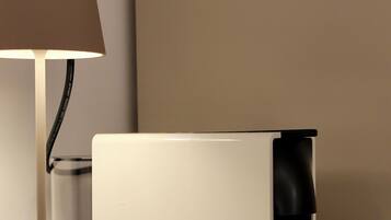 Een moderne lamp met een beige lampenkap en een cilindrische voet, geplaatst naast een wit rechthoekig object met een zwarte, cilindervormige onderdelen.
