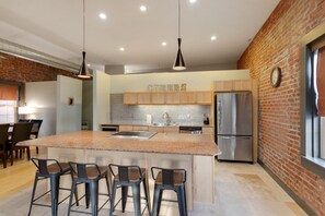 Una cocina moderna con una isla central, taburetes de bar, electrodomésticos de acero inoxidable y una pared de ladrillo decorativa.