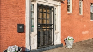 Un bâtiment en briques rouges avec une porte noire, le numéro 310, et deux plantes en pot.