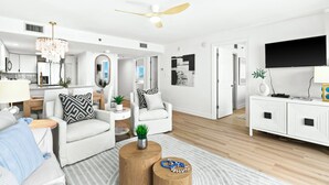 A modern living room with a sofa, armchair, coffee table, and a TV on a white cabinet.