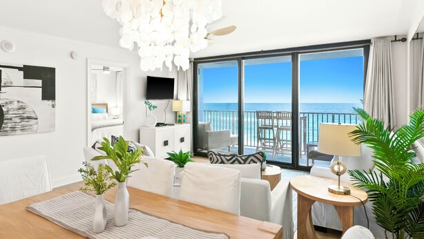A modern hotel room with a large balcony, a wooden dining table, and a chandelier.