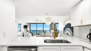 A modern kitchen with a central island, a built-in dishwasher, and a large window offering a view of the sea.