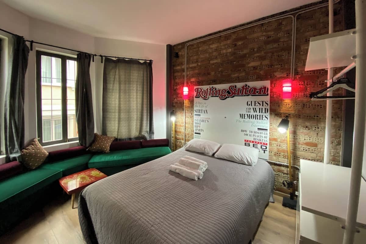 Une chambre d’hôtel avec un grand lit, un canapé vert, une table rouge et un mur en briques sur lequel est accroché un panneau.