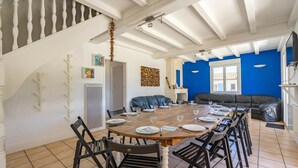 A dining area with a long table set for six, a black leather sofa, and a staircase with white balusters. - Villa 'Cap Mer 17' with Private Pool, Private Terrace and Wi-Fi (Saint-Palais-sur-Mer)