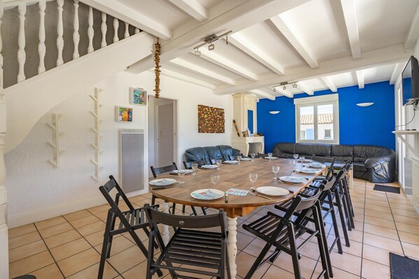A dining area with a long table set for six, a black leather sofa, and a staircase with white balusters.