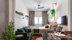 Ein modernes Wohnzimmer mit einer Couch, einem Esstisch gedeckt mit Gläsern, einem Deckenventilator und einem an der Wand befestigten Fernseher.