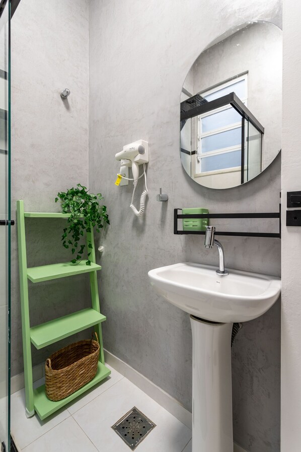 Une salle de bain avec un lavabo blanc, des étagères vertes, une plante suspendue, un sèche-cheveux et un miroir.