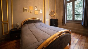 A bedroom with a bed, a nightstand, a dresser, a mirror, and a window with a view of trees. - Historic Boutique Apartment in Downtown Cairo (Cairo Governorate)