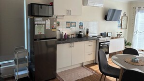 A compact kitchen with a refrigerator, stove, microwave, and a small dining area with a table and chairs. - Seascape Retreat: Time to Slow Down (Agnes Water)